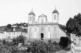 Fachada de igreja, com casario ao redor e parte de praça pública, na cidade natal de Oswaldo Cruz