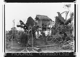Cientistas da expedição e americano sob construção apoiada em piloto de madeira, teto de palha e ...