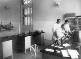 Oswaldo Cruz ao microscópio em laboratório de Manguinhos, observado por seu filho Bento Oswaldo C...