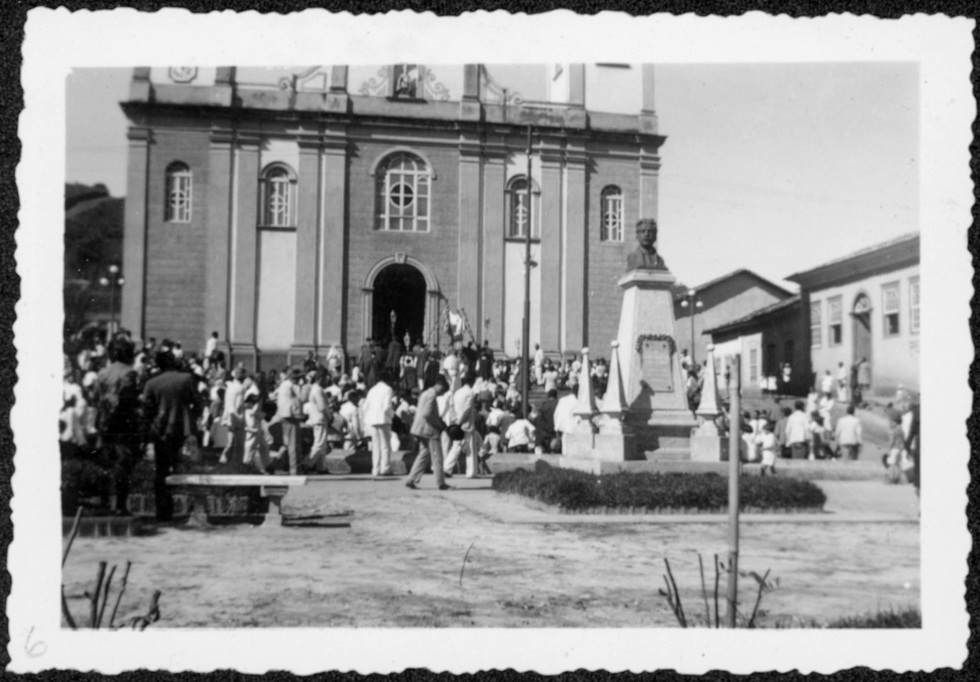 Chegada de procissão à igreja em primeiro plano busto de Oswaldo Cruz na praça da cidade